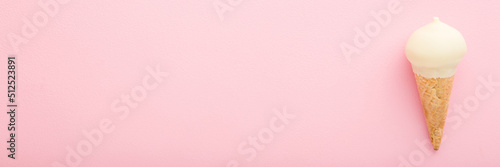 Waffle cone of white vanilla ice cream on light pink table background. Pastel color. Wide banner. Closeup. Cold sweet snack in summer. Empty place for text. Top down view.