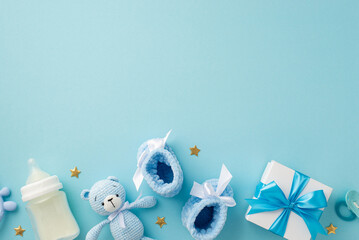 Baby accessories concept. Top view photo of giftbox knitted booties teddy-bear toy pacifier milk bottle and gold stars on isolated pastel blue background with copyspace
