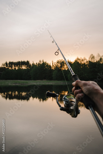 Man catching fish, pulling rod while fishing from lake or pond. Fisherman with rod, spinning reel on a boat. Sunrise. Fishing for pike, and perch. Background wild nature.