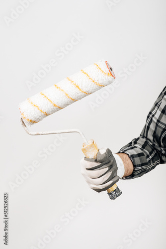 A male builder in a hard hat holds a paint roller on a white background, close-up