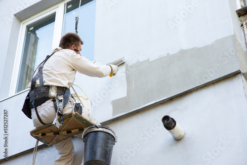 Builder-alpinist paints the facade of the building in a light color photo
