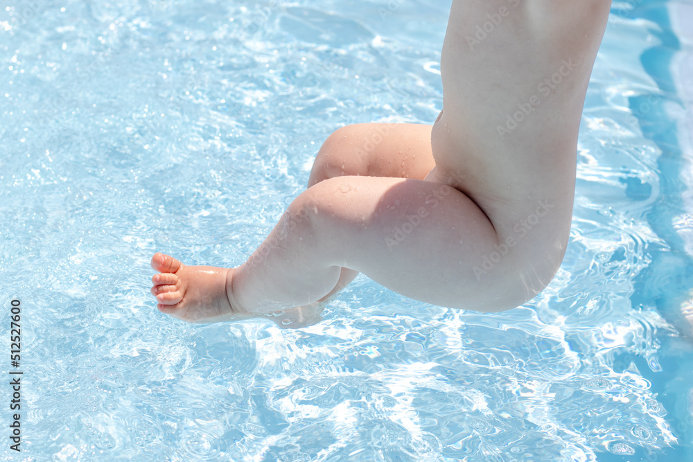 cute little baby legs in pool water or holding feet up,mother is in the back.steps in blue color water.family vacation concept.activities for kids.having fun
