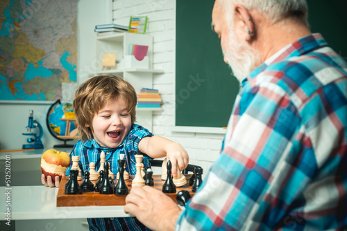 Grandson child boy with grandfather playing chess.