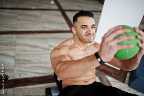 Muscular arab man training in modern gym. Fitness arabian men with naked torso doing exercises with ball.