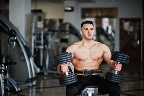 Muscular arab man training in with dumbbells modern gym. Fitness arabian men with naked torso doing workout . © AS Photo Family