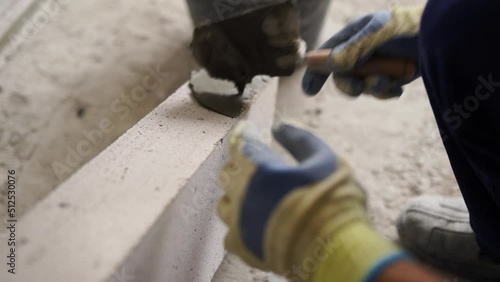 Bricklayer applies adhesive glue on autoclaved aerated concrete blocks with trowel and spatula. Brickwork worker contractor puts mortar on foam concrete doing masonry on construction site. photo