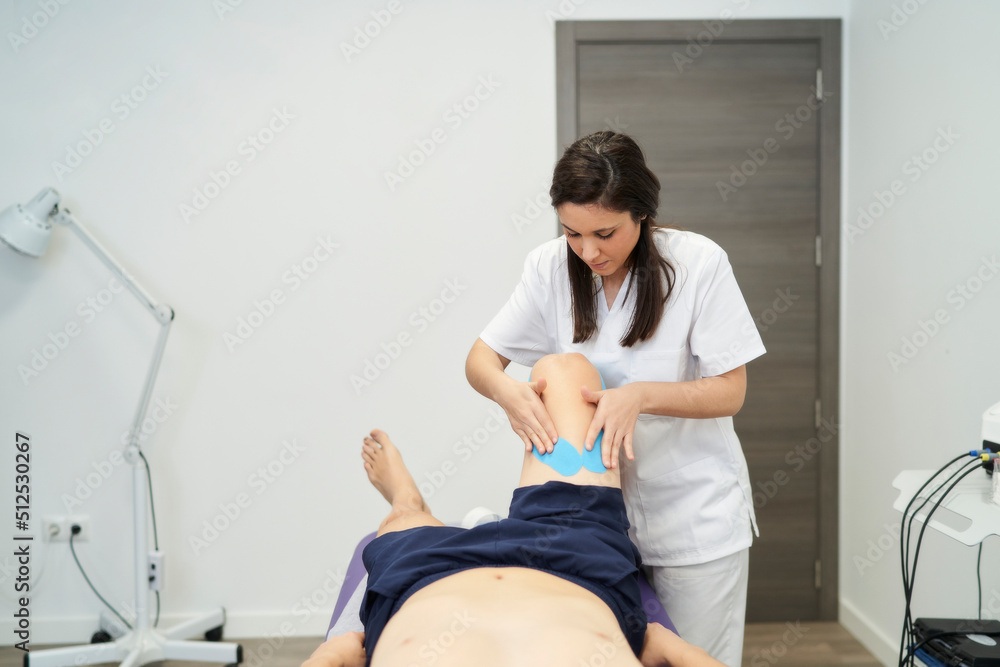 physiotherapist treating the patient's knee with neuromuscular taping physiotherapist treating the patient's knee with neuromuscular taping