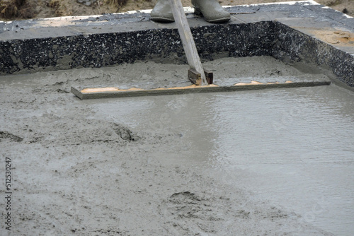  A building worker bull-floating the wet concrete