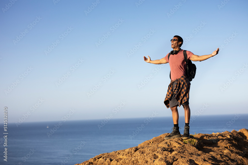 Young man standing on the stone with raised up arms. Tourist man on the top of the mountain Young man standing on the stone with raised up arms. Tourist man on the top of the mountain