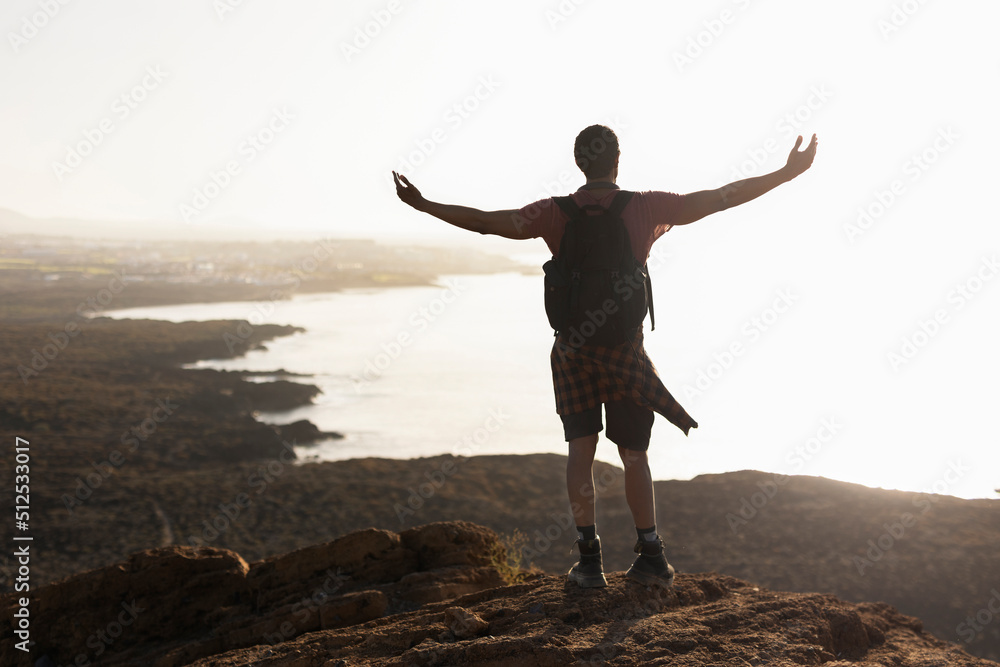 Young man standing on the stone with raised up arms. Tourist man on the top of the mountain