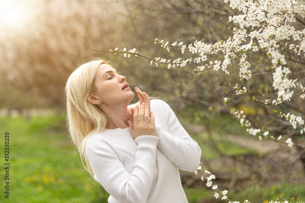 Woman allergic suffering from seasonal allergy at spring, posing in blossoming garden at springtime. Young woman sneezing in front of blooming tree. Spring allergy concept Woman allergic suffering from seasonal allergy at spring, posing in blossoming garden at springtime. Young woman sneezing in front of blooming tree. Spring allergy concept