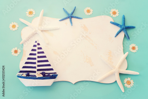 nautical concept with sail boat, seashells, star fish and blank board for copy space over mint blue wooden background photo