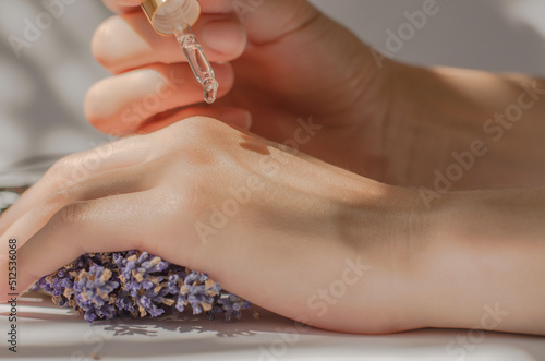 Female hands hold a pipette with lavender oil. Lavender oil dripping from a pipette on hands, close-up