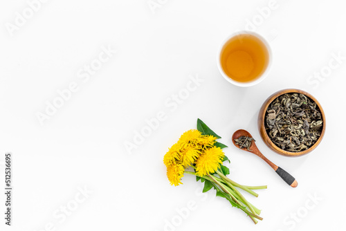 Yellow meadow dandelions with tea and dry leaves in bowl, top view