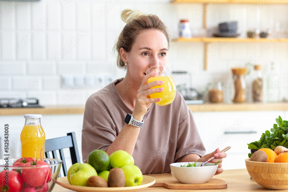 Healthy lifestyle. Beautiful happy woman drinking juice during breakfast. Beautiful female drink fresh juice and eating fresh salad while sitting in her kitchen. Vegan meal Healthy lifestyle. Beautiful happy woman drinking juice during breakfast. Beautiful female drink fresh juice and eating fresh salad while sitting in her kitchen. Vegan meal