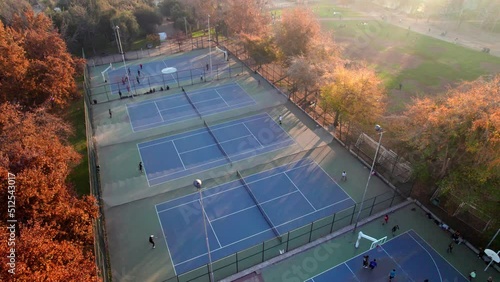 Aerial view of a group of people playing on a tennis court, trees in autumn, Parque Araucano, Santiago, Chile. photo