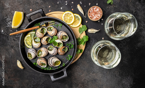 Fototapeta Naklejka Na Ścianę i Meble -  Fried snails Escargots de Bourgogne with herbs, butter, garlic on metal plate with forks, wine glass. gourmet food. Restaurant menu, dieting, cookbook recipe