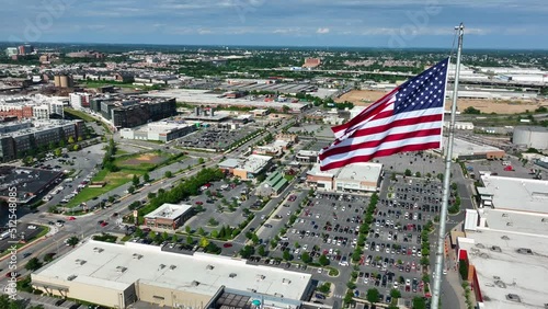 American flag proudly flies over urban city in USA. Retail shopping mall, office building, homes and houses. Aerial orbit. photo