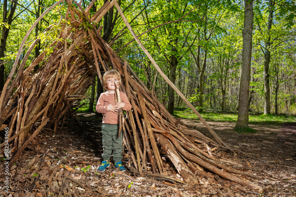 Blond boy with wood pile play in hut of branches Blond boy with wood pile play in hut of branches