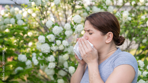 Caucasian woman suffers from allergies and blows her nose into a napkin while walking in the park. 