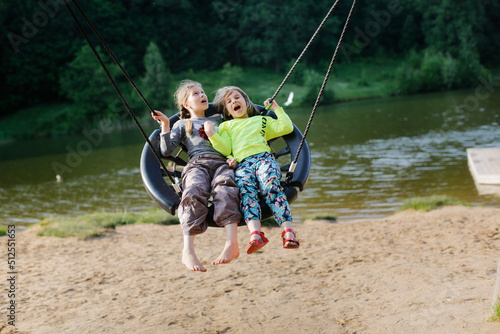 kids swinging on wicker swing on playground in park by lake, children's summer vacation with friends