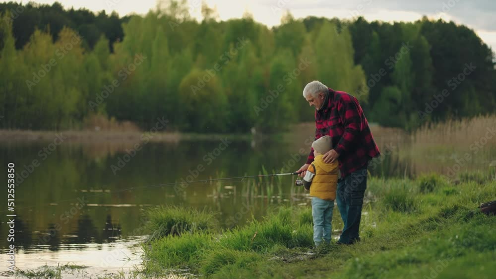 little boy is learning to fish on lake shore, loving grandfather is helping little boy is learning to fish on lake shore, loving grandfather is helping