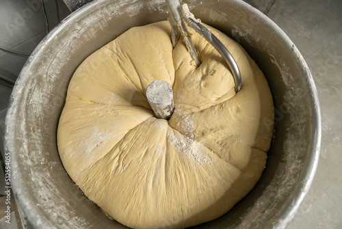 Fotografie Close-up of kneading elastic dough for bread in a kneading machine in a bakery