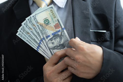 Business man holding dollar cash in hand hiding money in suit. Concept for corruption, finance profit, bail, crime, bribing, fraud.