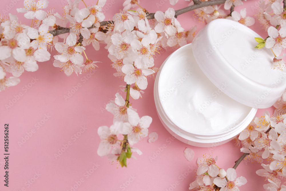 Container with bodycare and skincare cream on a pink background with blooming cherry. Cosmetic facial skin care and spa. Natural treatment concept. Container with bodycare and skincare cream on a pink background with blooming cherry. Cosmetic facial skin care and spa. Natural treatment concept.
