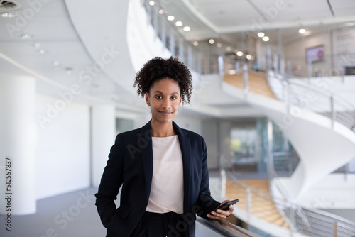 Portrait of African American businesswoman holding a smartphone in modern corporate office atrium photo