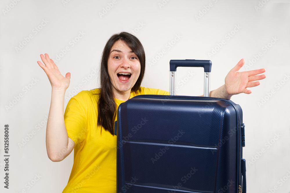 An enthusiastic woman with her mouth open spreads her arms to the sides in surprise sitting near a travel suitcase An enthusiastic woman with her mouth open spreads her arms to the sides in surprise sitting near a travel suitcase