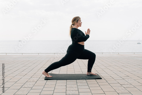 plus size girl practicing yoga in front of the ocean on a summer day