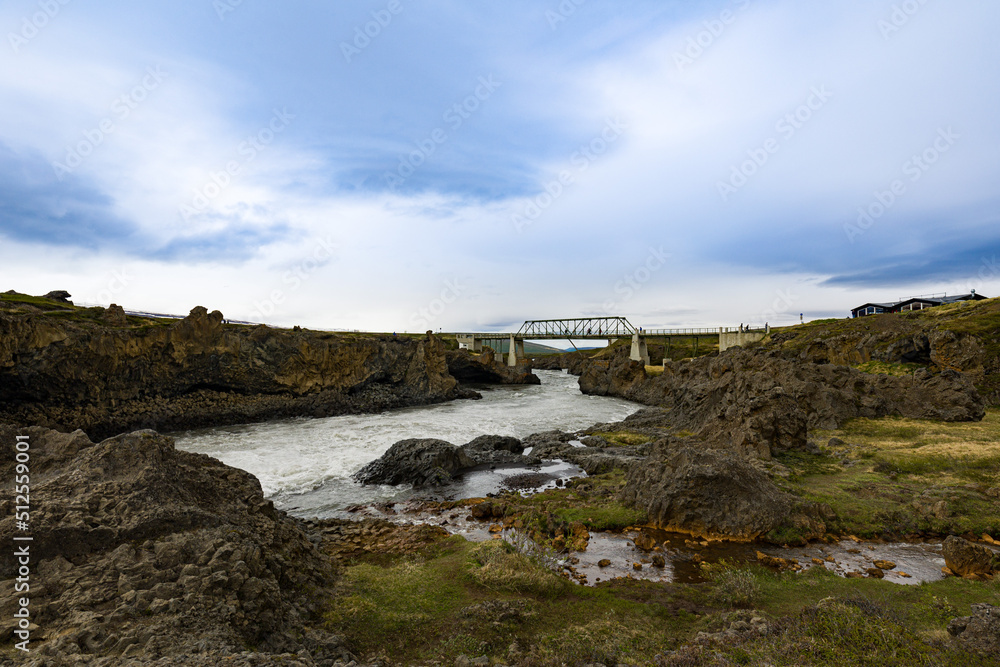 Small creek joining the force of a river near Icelandic waterfalls with a bridge between rock formations