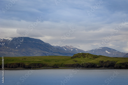 Majestic Icelandic landscape of horizontal stripes of body of water, grass colored hills and snow covered mountains
