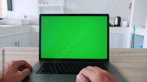 Laptop with green screen. Male hands typing and scrolling on a track pad. Man using computer at home on kitchen table