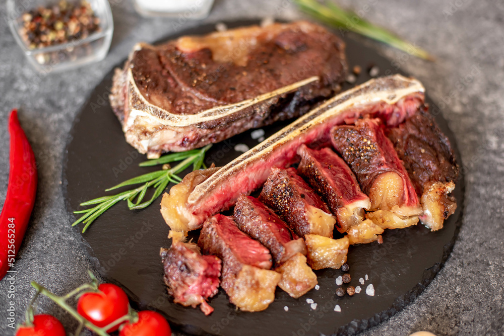 Grilled New York beef steak on the bone, herbs and spices on a stone background