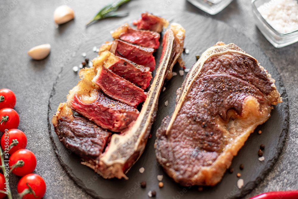 Grilled New York beef steak on the bone, herbs and spices on a stone background Grilled New York beef steak on the bone, herbs and spices on a stone background