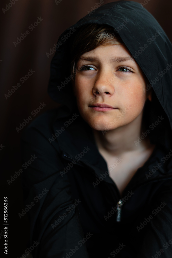 Portrait of blonde teenage boy on dark background outdoor. Low key close up shot of a young teen boy, adolescence. Selective focus. Loneliness, sadness, adolescent anxiety, emotional