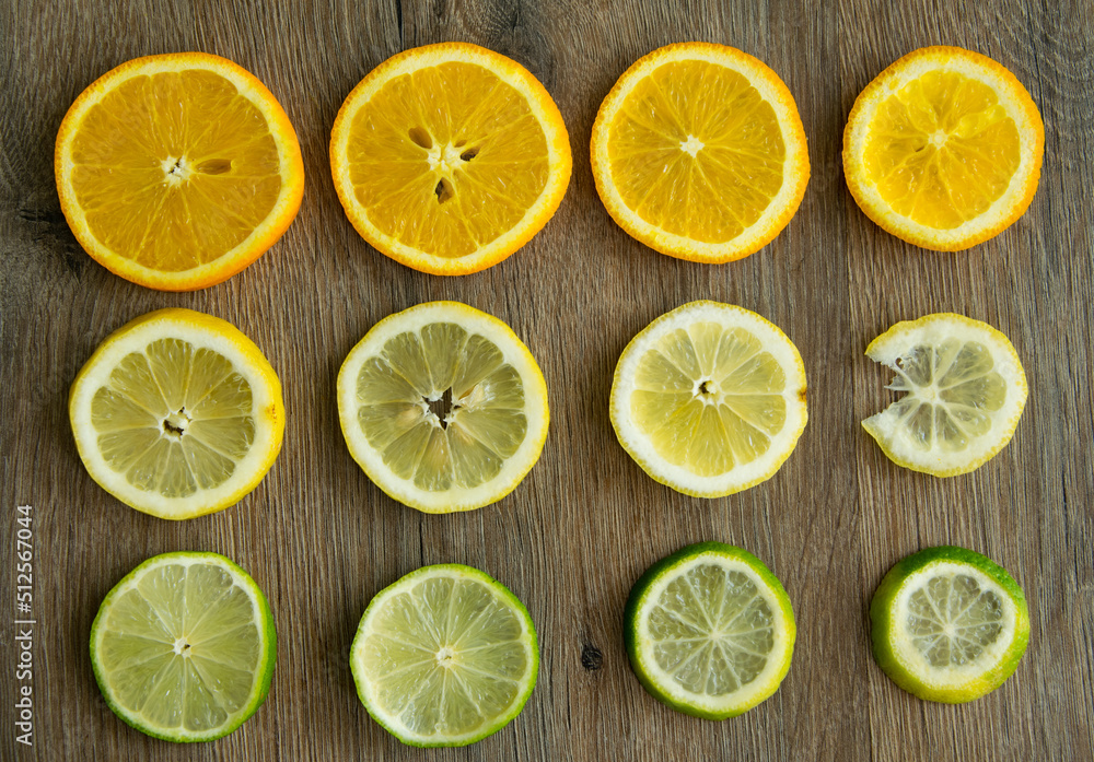 Picture of citrus fruits cut into round plates arranged in row on brown background. Ripe juicy fruit slices of orange, lemon, lime laid out in line on wooden table. Summer fresh light food