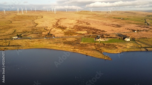 Aerial view of a lake with wind turbines in the distance surrounded by countryside. 