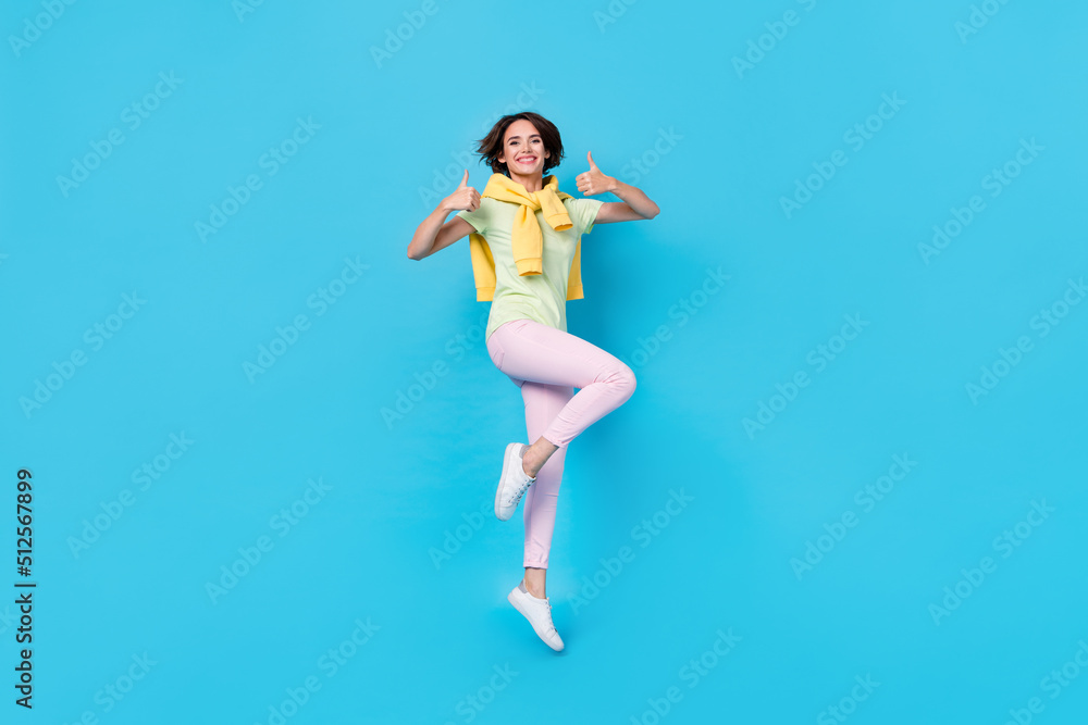 Full body photo of cute young brunette lady jump show thumb up wear t-shirt trousers footwear isolated on blue background