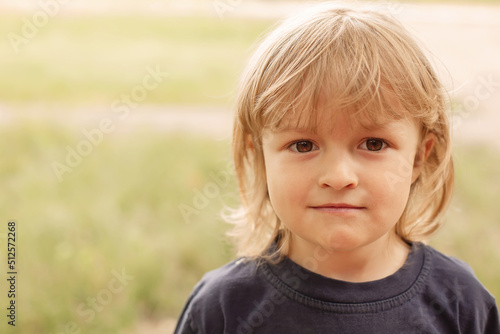 close-up portrait of the pensive face of a little blond boy on a green background summer street
