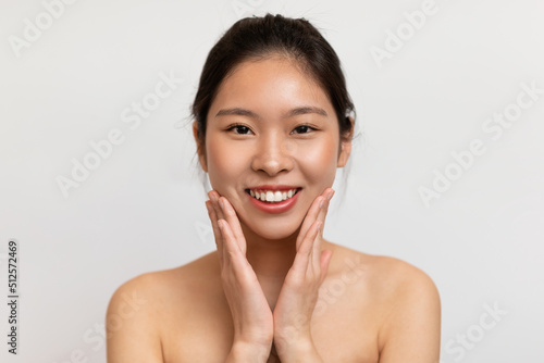Happy young asian lady touching her cheeks and smiling at camera, korean woman enjoying skincare treatments