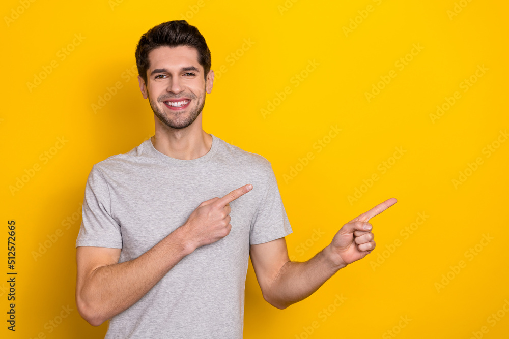 Photo of nice brunet millennial guy index empty space wear grey t-shirt isolated on yellow color background Photo of nice brunet millennial guy index empty space wear grey t-shirt isolated on yellow color background