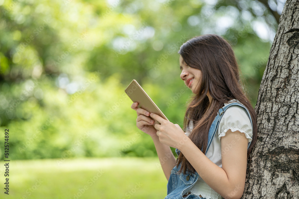 Thoughtful smile woman in park using smart digital tablet, Portrait of a young charming business woman checking online Business work on her smart tablet or labtop outdoors in the park on soft green Thoughtful smile woman in park using smart digital tablet, Portrait of a young charming business woman checking online Business work on her smart tablet or labtop outdoors in the park on soft green