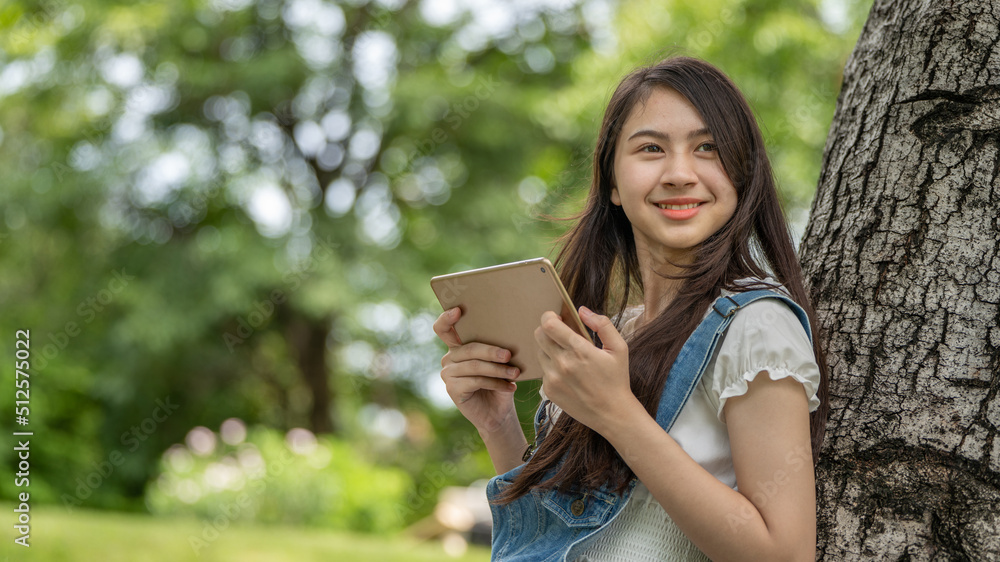 Thoughtful smile woman in park using smart digital tablet, Portrait of a young charming business woman checking online Business work on her smart tablet or labtop outdoors in the park on soft green Thoughtful smile woman in park using smart digital tablet, Portrait of a young charming business woman checking online Business work on her smart tablet or labtop outdoors in the park on soft green