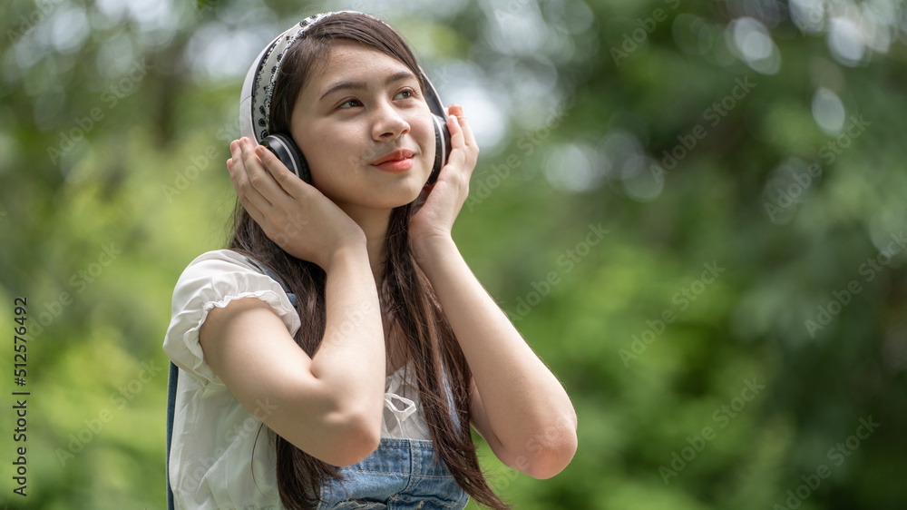 Beautiful young woman girl in beige shirt posing in Green city Park background , Smile girl Listening Music with Headphones feeling Touching Happiness. People lifestyle concept. Mock up copy space Beautiful young woman girl in beige shirt posing in Green city Park background , Smile girl Listening Music with Headphones feeling Touching Happiness. People lifestyle concept. Mock up copy space
