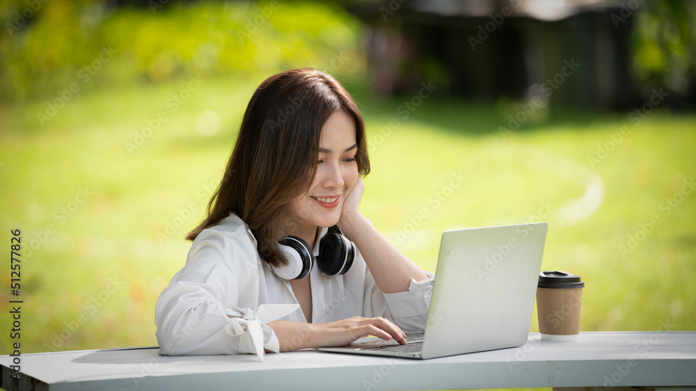 Thoughtful smile Happy woman videocalling online or meeting online working with a laptop in a park Thoughtful smile Happy woman videocalling online or meeting online working with a laptop in a park
