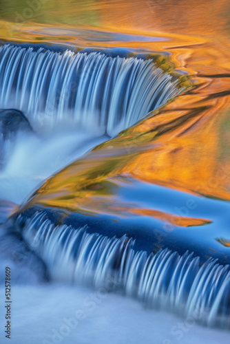 Landscape of a Bond Falls cascade captured with motion blur and illuminated by reflected color from sunlit autumn maples and blue sky overhead, Ottawa National Forest, Michigan's Upper Peninsula, USA