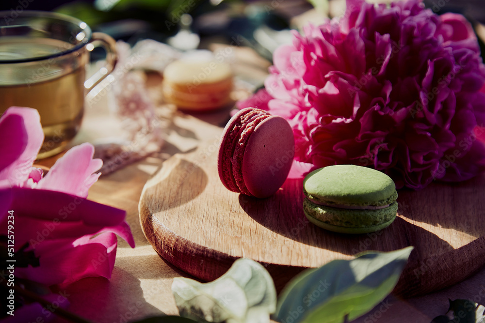 Bright macarons dessert and herbal tea for brunch outside in the terrace. Blooming pink peony flowers under trendy hard shadows. Relaxation, thoughtful, meditative, good mood lifestyle
